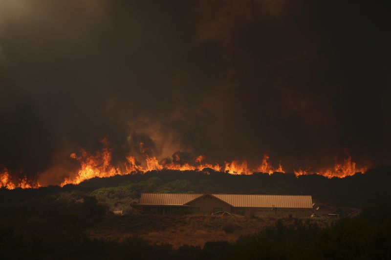 The Airport Fire crests over a structure Tuesday, Sept. 10, 2024, in El Cariso, an unincorporated community in Riverside County, Calif. (AP Photo/Eric Thayer)