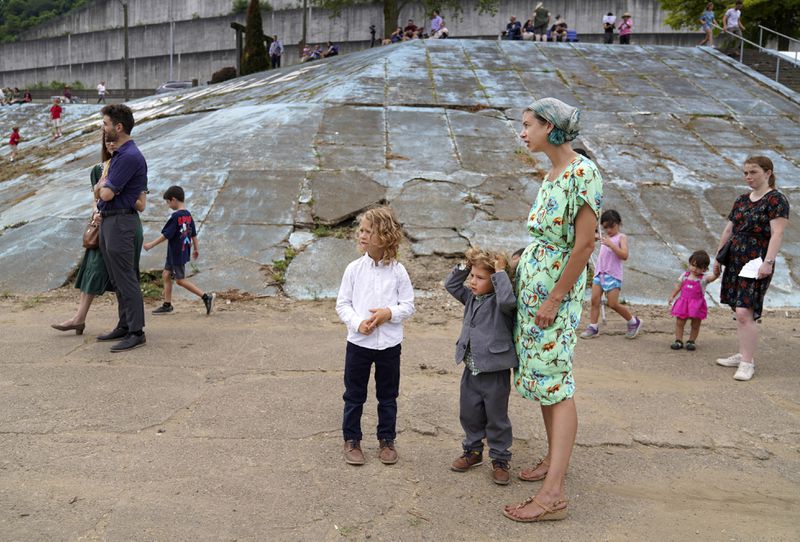 Misha McGovern, right, and her two sons, Benedict, center, and Bede, left, stand at the Steubenville Marina with fellow Catholics awaiting the arrival of the Eucharist, in Steubenville, Ohio, Sunday, June 23, 2024. (AP Photo/Jessie Wardarski)