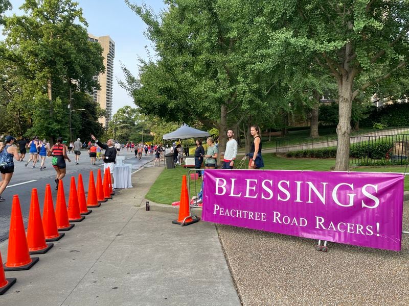 The Rev. Sam Candler of the Cathedral of St. Philip blesses runners with holy water during The Atlanta Journal-Constitution Peachtree Road Race on Saturday, July 3, 2021. (Photo: Anjali Huynh/AJC)