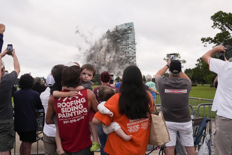 Tuff Gary, left, and Morgan LeBlanc with their children Hudson, Tuff, Jr., and Zander, of Jenning, La., watch the implosion of the Hertz Tower, that was heavily damaged after Hurricanes Laura and Delta in 2020 in Lake Charles, La., Saturday, Sept. 7, 2024. (AP Photo/Gerald Herbert)