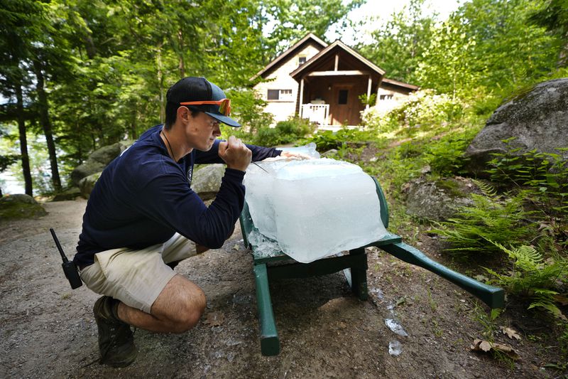 On the hottest day of the young summer season, Nate Lord uses an ice pick to break a block of ice before delivering it to a guest cabin at Rockywold Deephaven Camps, Thursday, June 20, 2024, in Holderness, N.H. Ice harvested from Squam Lake during the winter is used for refrigeration at each cabin throughout the summer. (AP Photo/Robert F. Bukaty)