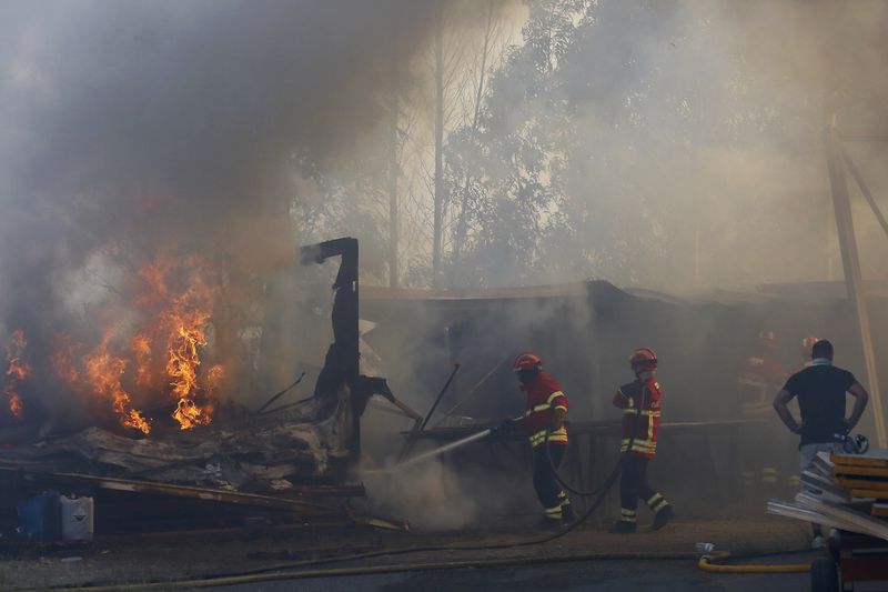 Firefighters work to control a fire next to warehouses in Sever do Vouga, a town in northern Portugal that has been surrounded by forest fires, Monday, Sept. 16, 2024. (AP Photo/Bruno Fonseca)