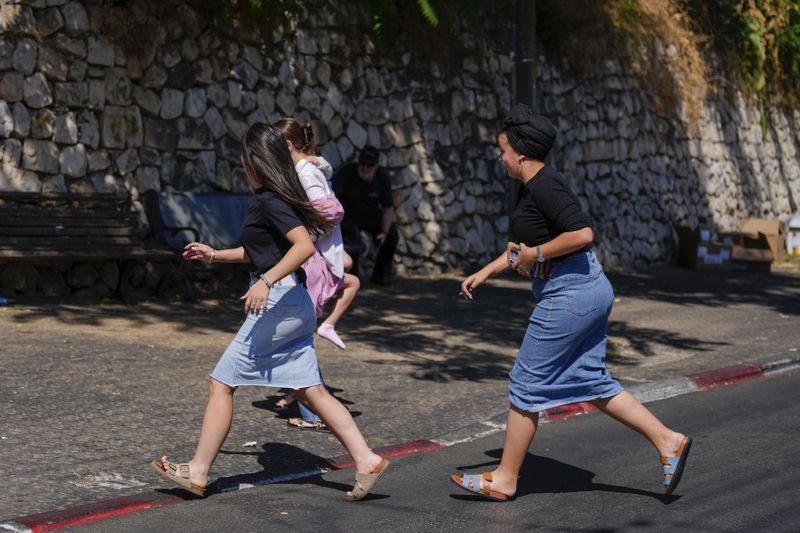 People run to take cover as a siren sounds a warning of incoming rockets fired from Lebanon, in Safed, northern Israel, Thursday, Sept. 26, 2024. (AP Photo/Ariel Schalit)