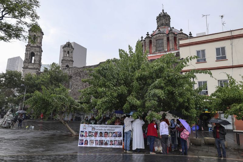 Anglican priest Rev. Arturo Carrasco stands with Benita Ornelas, in red, and her husband Marcos, as they pass out tacos after holding a Mass on the fifth anniversary of the disappearance of the couple's son Fernando Ivan Ornelas in Mexico City, Sunday, July 21, 2024. Benita and Marcos are members of the search collective "Uniendo Esperanzas" or Uniting Hope. (AP Photo/Ginnette Riquelme)