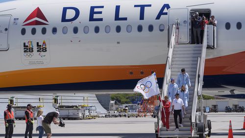 Los Angeles Mayor Karen Bass carrying the Olympic flag, LA28 chairman Casey Wasserman, front right, and Team USA Olympians, skateboarder Tate Carew, second from left, diver Delaney Schnell, rear right, and volleyball player Micah Ma'a, top right, arrive at Los Angeles International Airport, Monday, Aug. 12, 2024. (AP Photo/Damian Dovarganes)