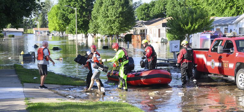 Tam Nguyen, wearing cap, is helped to dry land by a Sioux City Fire Rescue firefighter after he and Bruce Ege, left, were rescued by boat from their flooded homes in the Riverside neighborhood of Sioux City, Iowa, Monday, June 24, 2024. The evacuations were occurring in the wake of flooding from the Big Sioux and Missouri Rivers. (Tim Hynds/Sioux City Journal via AP)