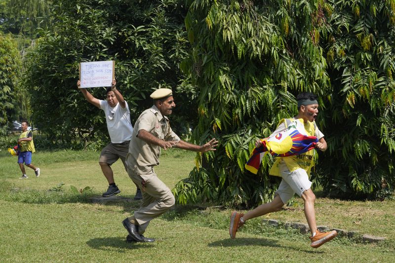 An Indian policeman runs after an exile Tibetan to detain him as others shout slogans against the human rights situation in Tibet during a protest to coincide China marking its 75th year of Communist Party rule, outside Chinese embassy, in New Delhi, India, Tuesday, Oct. 1, 2024. (AP Photo/Manish Swarup)