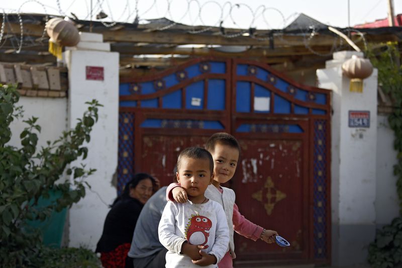 FILE - Uyghur children play while their relatives rest outside their house, decorated with Chinese lanterns and barbed wire at the Unity New Village in Hotan, in western China's Xinjiang region on Sept 20, 2018. Authorities in China's western Xinjiang region have been systematically replacing the names of villages inhabited by Uyghurs and other ethnic minorities to reflect the ruling Communist Party's ideology, as part of an attack on their cultural identity, according to a report released Wednesday, June 19, 2024, by Human Rights Watch. (AP Photo/Andy Wong, File)