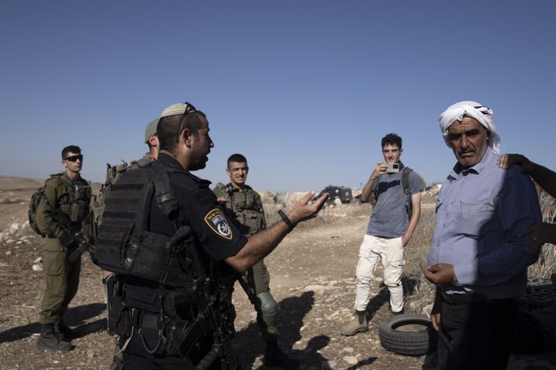 Israeli Police speak to residents of the West Bank village of Khirbet Zanuta, after activists called to report Israeli setters in the village,Thursday, Aug. 29, 2024. Ten months after settlers threatened to kill them if they didn't leave their village, some Palestinian residents are finally home, under a rare court order. (AP Photo/Maya Alleruzzo)