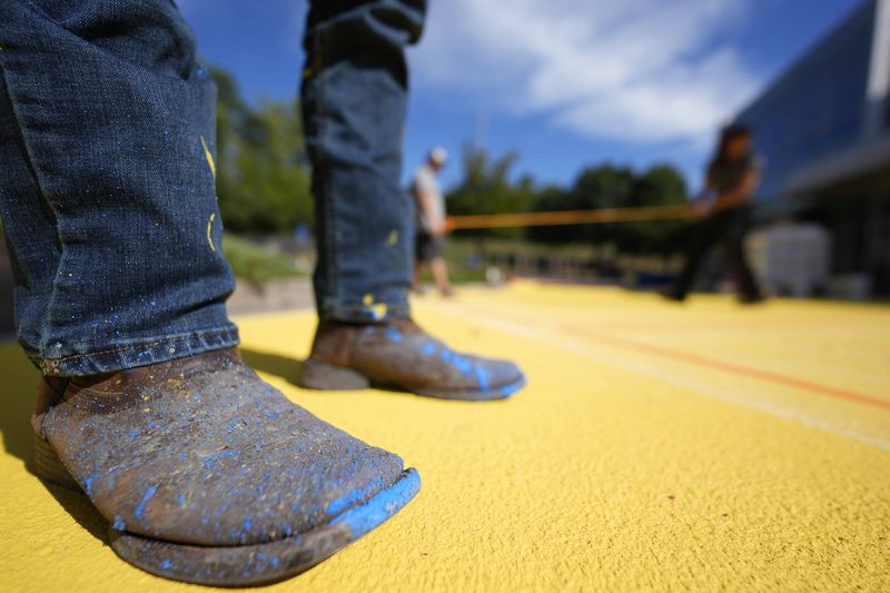 Ronnie Jefferies works on the parking lot at Science, Arts and Entrepreneurship School where it is being repainted to help cool it by making it more reflective, Wednesday, Sept. 4, 2024, in Mableton, Ga. (AP Photo/Mike Stewart)