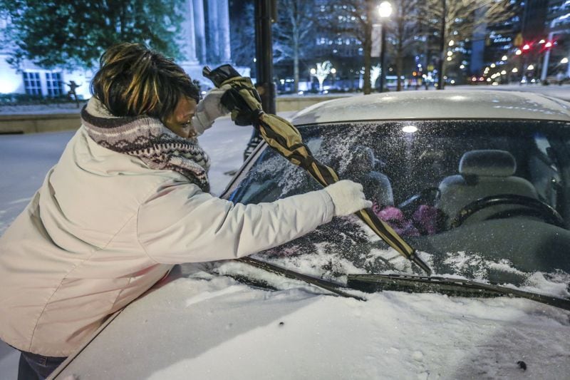 Jennifer Mahone uses her umbrella to clear snow and ice from her car on Peachtree Street near the High Museum on Wednesday. The snow subsided before noon, but the number of crashes did not. JOHN SPINK/JSPINK@AJC.COM