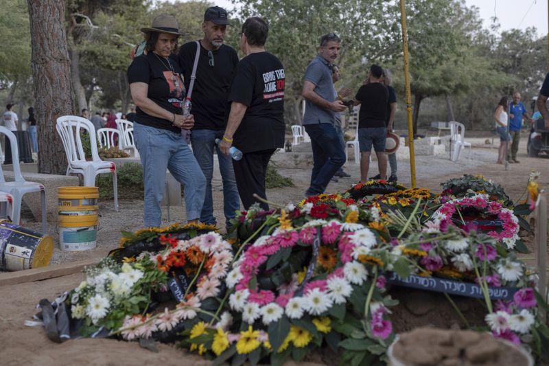 Keren Munder, the daughter of Avraham Munder, who was killed in Hamas captivity in the Gaza Strip and recovered by the Israeli military in Gaza, stands next to his grave at Kibbutz Nir Oz, southern Israel, Wednesday, Aug. 21, 2024. Her brother, Roee Munder, who was killed on Oct. 7, 2023, was reburied at the Kibbutz. (AP Photo/Ohad Zwigenberg)