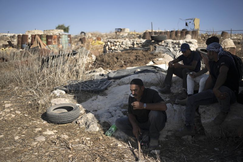 Palestinians rest in the shade in the West Bank village of Khirbet Zanuta, Thursday, Aug. 29, 2024. Ten months after settlers threatened to kill them if they didn't leave their village, some Palestinian residents are finally home, under a rare court order. (AP Photo/Maya Alleruzzo)