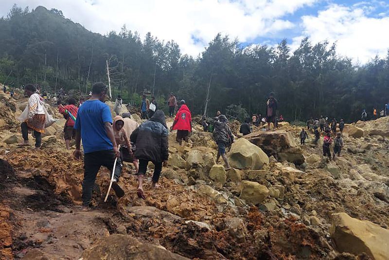 In this photo provides the International Organization for Migration, people cross over the landslide area to get to the other side in Yambali village, Papua New Guinea, Friday, May 24, 2024. More than 100 people are believed to have been killed in the landslide that buried a village and an emergency response is underway, officials in the South Pacific island nation said. The landslide struck Enga province, about 600 kilometers (370 miles) northwest of the capital, Port Moresby, at roughly 3 a.m., Australian Broadcasting Corp. reported. (Benjamin Sipa/International Organization for Migration via AP)