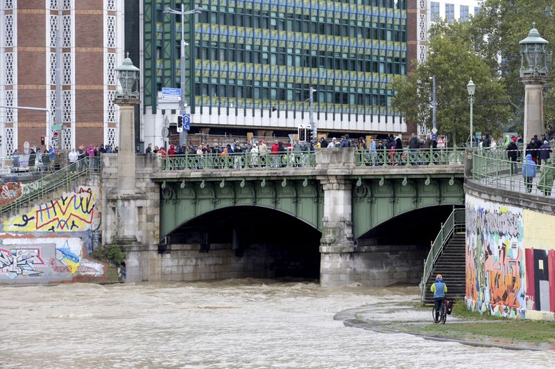 People watch the junction of river Wien and Donaukanal channel as they flood their banks in central Vienna, Austria, Sunday, Sept. 15, 2024. (AP Photo/Heinz-Peter Bader)