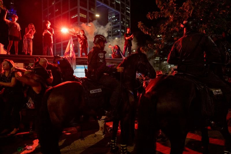 Demonstrators light flares as police on horses block their way during a protest demanding a cease-fire deal and the immediate release of hostages held by Hamas in the Gaza Strip on Thursday, Sept. 5, 2024, in Tel Aviv, Israel. (AP Photo/Ohad Zwigenberg)