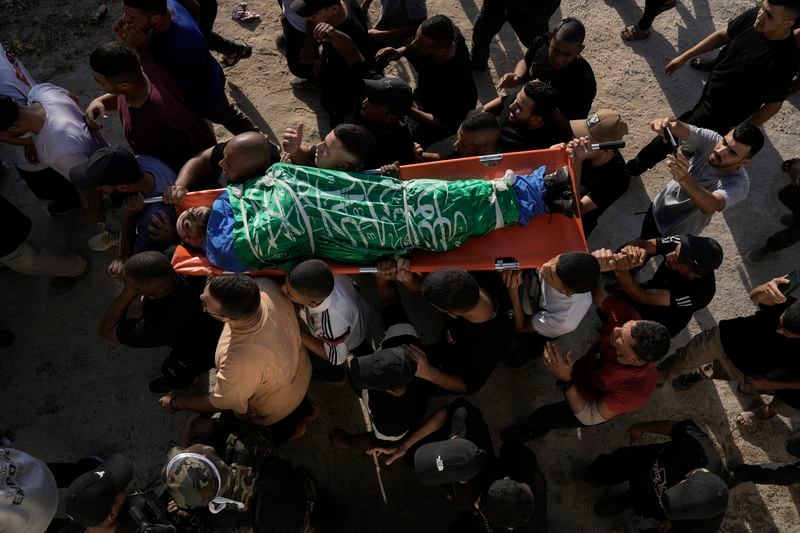 Mourners carry body of Muawiyah Hajj Ahmed, wrapped with Hamas flag, during the funeral of three Palestinians who were killed by an Israeli airstrike in the occupied West Bank refugee camp of Tulkarem, Thursday, Aug. 22, 2024. The Palestinian Health Ministry says three people have been killed in an Israeli strike in the occupied West Bank. (AP Photo/Majdi Mohammed)