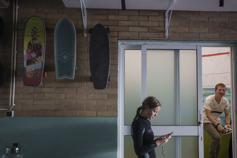 Surf Church member Uliana Yarova checks her phone after catching waves, while her brother Zakharii Yarovyi, changes clothes ahead of a worship service at the church in the suburbs of Porto, Portugal on Sunday, Aug. 18, 2024. (AP Photo/Luis Andres Henao)