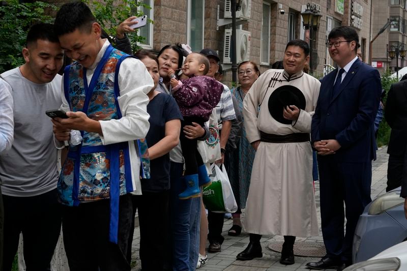 Mongolian Prime Minister Oyun-Erdene Luvsannamsrai, second from right, dressed in Mongolian traditional garment called deel, reacts as a woman takes a selfie with her child as they wait in line outside a polling station in Ulaanbataar, Mongolia, Friday, June 28, 2024. Voters in Mongolia are electing a new parliament on Friday in their landlocked democracy that is squeezed between China and Russia, two much larger authoritarian states. (AP Photo/Ng Han Guan)