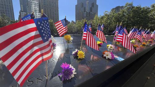 Flags and flowers are placed by the names of those killed during the Sept. 11, 2001, attacks at the reflecting pools at the National September 11 Memorial & Museum, Tuesday, Sept. 10, 2024, in New York. (AP Photo/Donald King)