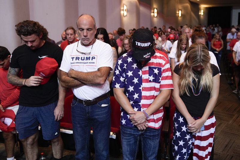 Audience members stand and pray before Republican presidential candidate former President Donald Trump arrives to deliver remarks on the tax code, and manufacturing at the Johnny Mercer Theatre Civic Center, Tuesday, Sept. 24, 2024, in Savannah, Ga. (AP Photo/Evan Vucci)