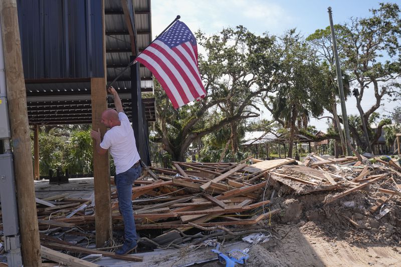 John Taylor puts up an American flag on his destroyed property in the aftermath of Hurricane Helene, in Horseshoe Beach, Fla., Saturday, Sept. 28, 2024. (AP Photo/Gerald Herbert)