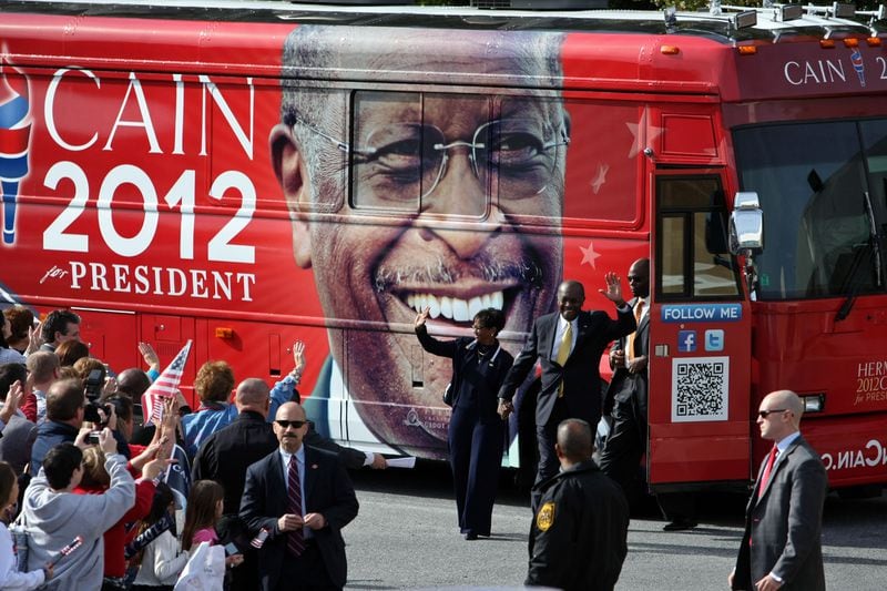 Herman Cain walks with his wife, Gloria, as he exits his campaign bus before he announced the suspension of his campaign for president. (AJC file/Jason Getz)