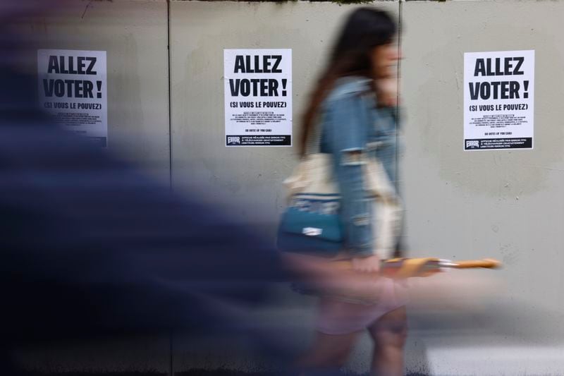 A woman walks past poster reading "Vote" ahead of the second round of the legislative election, Thursday, July 4, 2024 in Strasbourg, eastern France. French President Emmanuel Macron called the surprise legislative election on June 9 after his centrist alliance suffered a punishing defeat at the hands of the National Rally in French voting for the European Parliament. (AP Photo/Jean-Francois Badias)