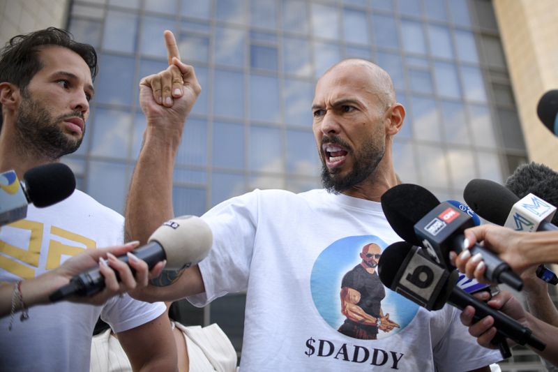 Andrew Tate speaks to media, next to his brother Tristan, left, outside the Bucharest Tribunal after being placed under house arrest, in Bucharest, Romania, Thursday, Aug. 22, 2024. A court in Romania's capital on Thursday placed the divisive internet influencer Andrew Tate under house arrest for 30 days, as prosecutors investigate a sprawling new case that involves allegations of human trafficking of minors and sex with a minor. (AP Photo/Alexandru Dobre)