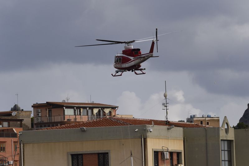 An Italian Firefighters helicopter flies over houses near the harbor of Porticello, southern Italy, Tuesday, Aug. 20, 2024, as rescue teams and divers returned to the site of a storm-sunken superyacht to search for six people, including British tech magnate Mike Lynch, who are believed to be still trapped in the hull 50 meters (164-feet) underwater. (AP Photo/Salvatore Cavalli)