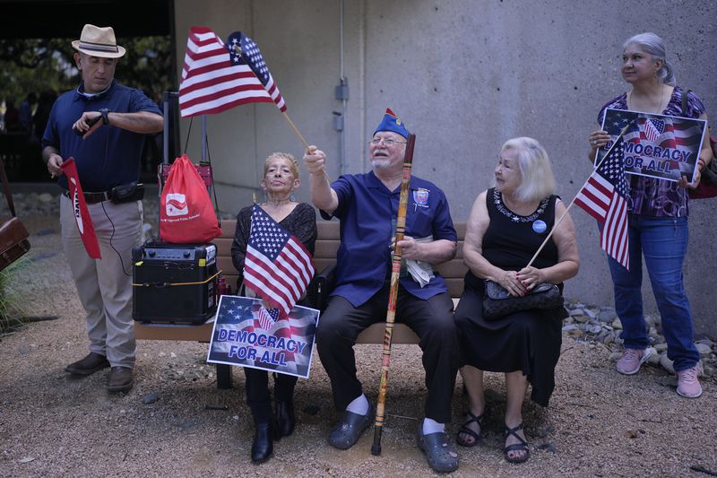 Roman Rena, center, waves a flag at a news conference where Officials with the League of United Latin American Citizens, or LULAC, held a news conference to respond to allegations by Texas Attorney General Ken Paxton, Monday, Aug. 26, 2024, in San Antonio. (AP Photo/Eric Gay)