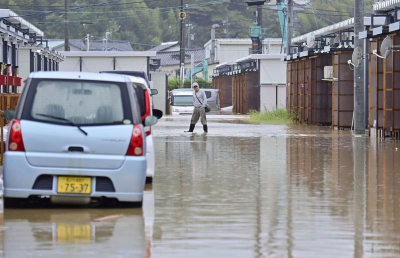 A man wades through a flooded street near temporary housing units installed after the Jan. 1 earthquake in Wajima, Japan, Sunday, Sept. 22, 2024, following heavy rain in central Japan's Noto peninsula area, where a devastating earthquake took place on Jan. 1. (Muneyuki Tomari/Kyodo News via AP)