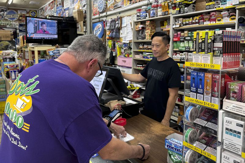 Richard Smith, right, who had to run his New Orleans store Adams Street Grocery Deli with a generator until power returned Friday afternoon, Sept. 13, 2024, helps a customer. (AP Photo/Jack Brook)