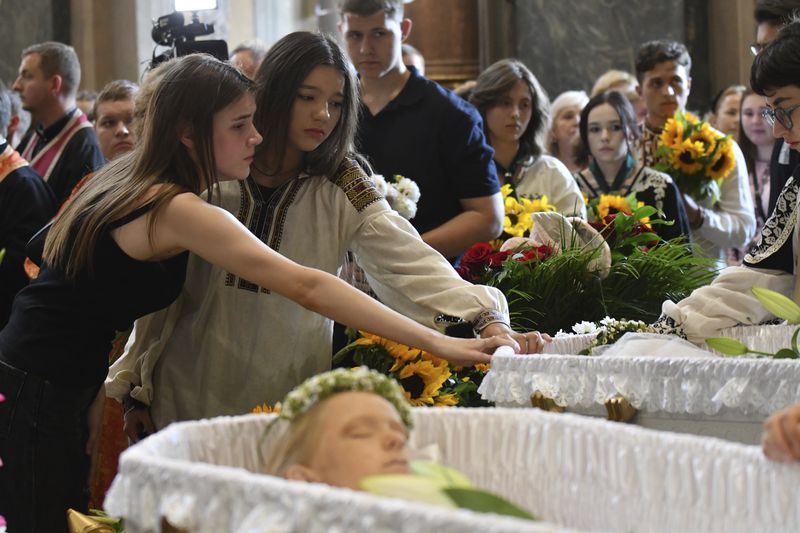 People mourn near the coffins of Yaroslav Bazylevych's family during the funeral service in the Garrison Church in Lviv, Ukraine, Friday, Sept. 6, 2024. Bazylevych's wife Yevgenia and their three daughters - Darina, 18, Emilia, 7, and Yaryna, 21 - were killed in Wednesday's Russian missile attack. (AP Photo/Mykola Tys)