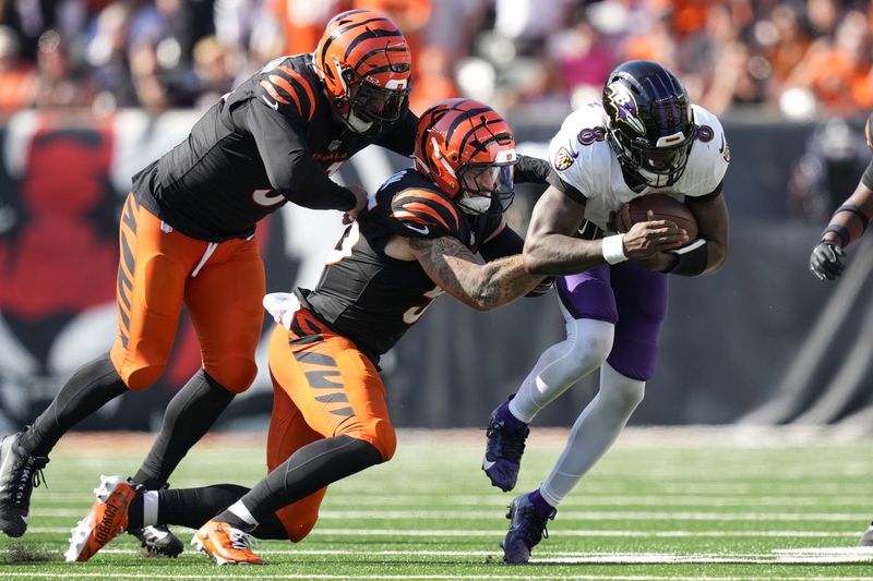 Baltimore Ravens quarterback Lamar Jackson=, right, runs with the ball as Cincinnati Bengals defensive end Trey Hendrickson, left, and linebacker Logan Wilson try to stop him during the second half of an NFL football game, Sunday, Oct. 6, 2024, in Cincinnati. (AP Photo/Carolyn Kaster)