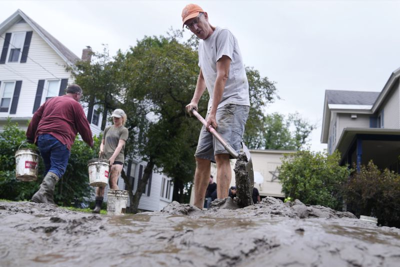 Homeowner Scott Mackie, right, shovels mud away from his home while cleaning up the remnants of Hurricane Beryl, Thursday, July 11, 2024, in Waterbury, Vt. Mackie said his basement was filled with nearly five feet of the muddy mixture, which friends and neighbors are helping to empty. (AP Photo/Charles Krupa)