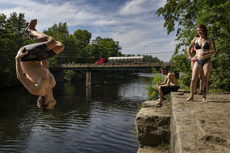 Levi Rush does a backflip off an old bridge abutment into the Saco River in Buxton, Maine, Tuesday, June 18, 2024. Hot weather is predicted until the end of the week. (Troy R. Bennett/The Bangor Daily News via AP)