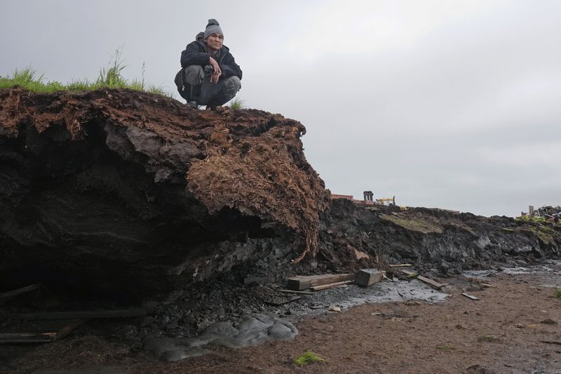 Charles Alexie stands along the coastal erosion that has eaten away at the riverbanks on Friday, Aug. 16, 2024, in Newtok, Alaska. (AP Photo/Rick Bowmer)