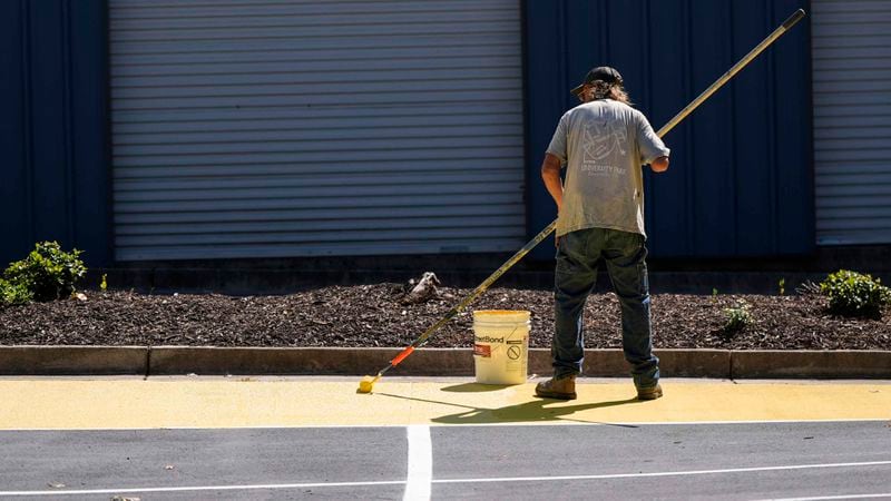 Ronnie Jefferies paints the parking lot at Science, Arts and Entrepreneurship School to help cool it by making it more reflective, Wednesday, Sept. 4, 2024, in Mableton, Ga. (AP Photo/Mike Stewart)