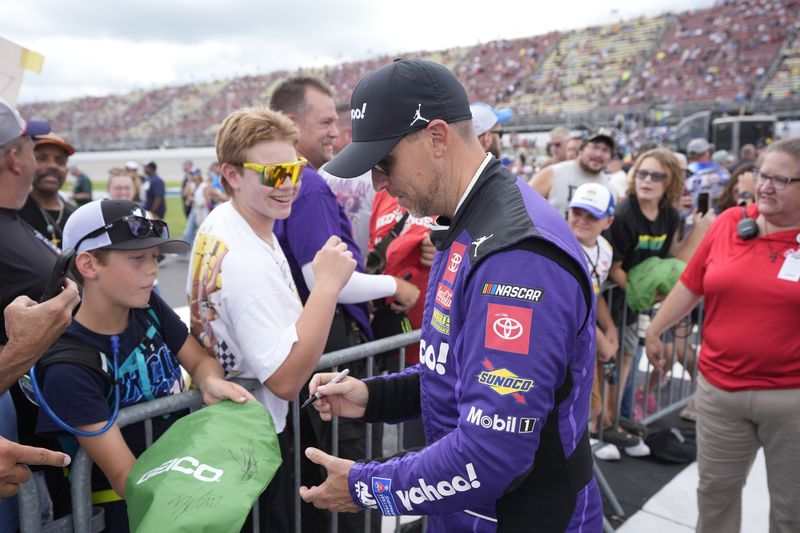 Denny Hamlin signs autographs before driver introductions of a NASCAR Cup Series auto race at Michigan International Speedway, Sunday, Aug. 18, 2024, in Brooklyn, Mich. (AP Photo/Carlos Osorio)