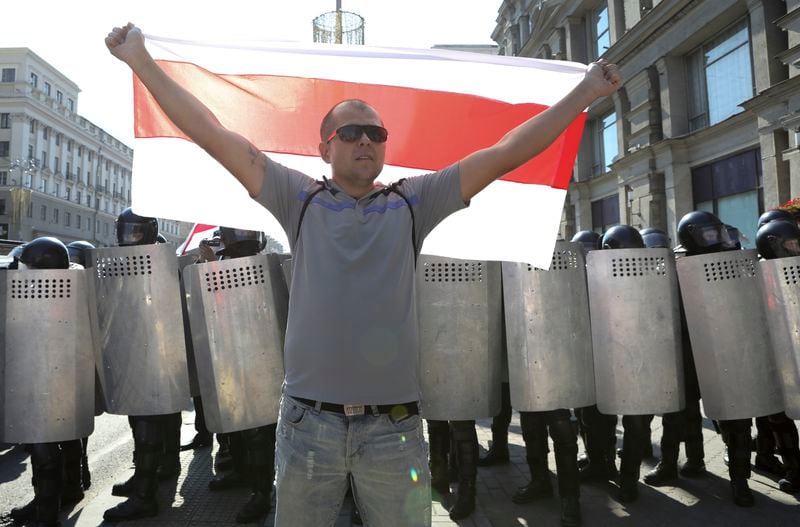 FILE – A protester holds a red-and-white flag that was a symbol of the opposition in front of a police line during an anti-government demonstration in Minsk, Belarus, on Aug. 30, 2020.(AP Photo, File)