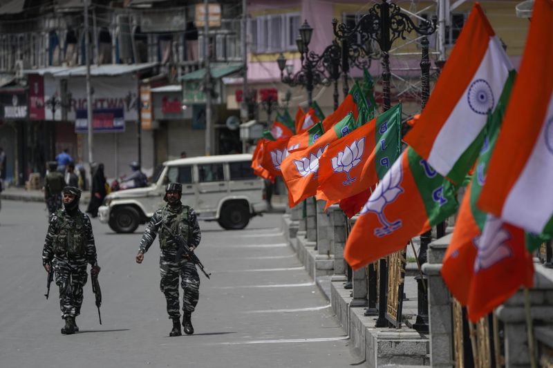 Indian security forces walk past Indian flags and flags of India's ruling Bharatiya Janata Party (BJP) as a motorcycle rally by BJP youth wing to the Kargil War Memorial passes through Srinagar, Indian controlled Kashmir, Monday, July 25, 2022. (AP Photo/Mukhtar Khan, File)