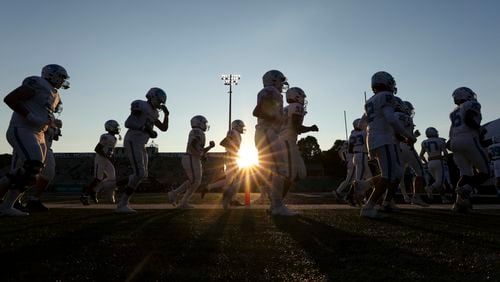 The sun sets as Seckinger football players run to return to their locker room briefly before their game against Roswell at Roswell High School, Friday, Sept. 20, 2024, in Roswell, Ga. (Jason Getz / AJC)

