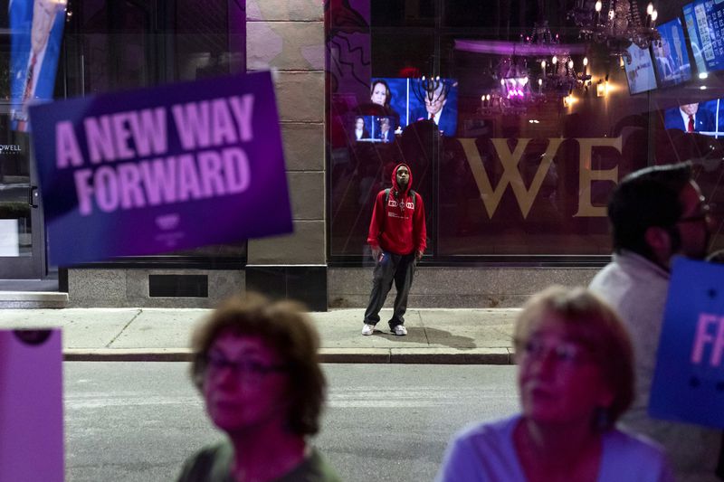 A pedestrian stops to watch a television across the street at Alley Cat showing the presidential debate between Republican presidential nominee former President Donald Trump and Democratic presidential nominee Vice President Kamala Harris, Tuesday, Sept. 10, 2024, in Providence, R.I. (AP Photo/David Goldman)