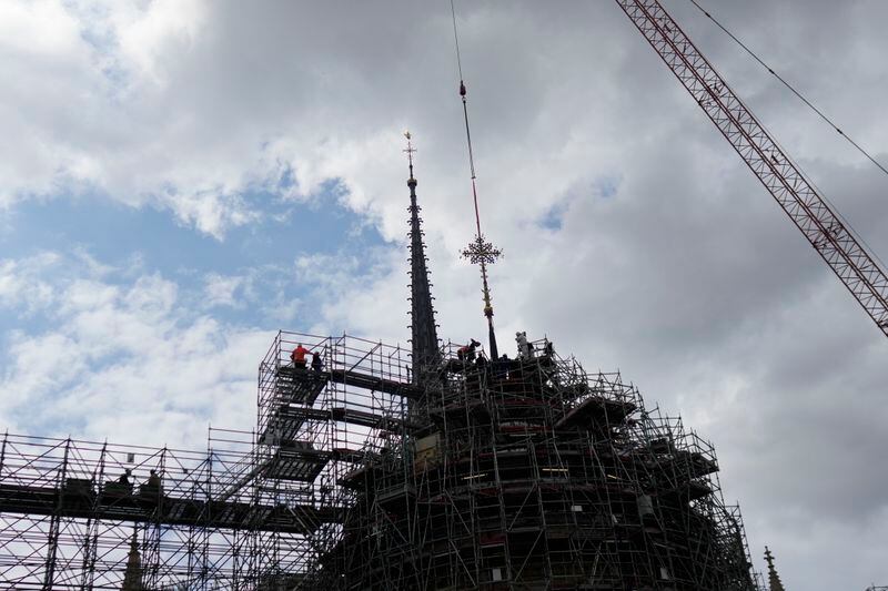 Workers install Notre Dame de Paris cathedral's Croix du Chevet in front of the cathedral spire, left, to be reinstalled Friday, May 24, 2024, in Paris. The Croix du Chevet is the only piece of the cathedral roof that did not burn in the devastating April 2019 fire. (AP Photo/Thibault Camus)