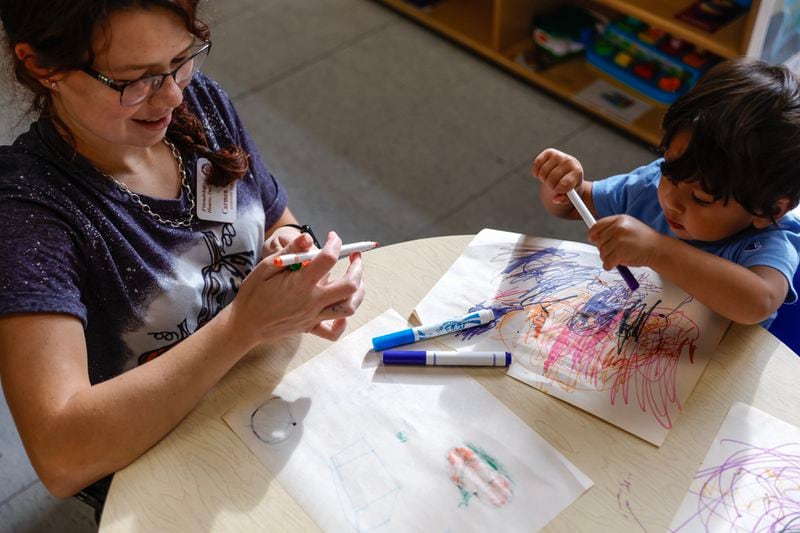 Carmen Wheat, an assistant teacher in the 1-year-old class at Friendship House Daycare in Dalton, Ga. helps a student draw. (Natrice Miller/ Natrice.miller@ajc.com)