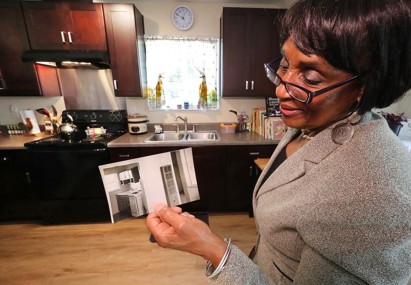 Canary Gordon, 72, shows a photo of her former public housing unit kitchen featuring a wall heater, small gas stove & sink she occupied since 1951 while standing in the kitchen of her new Thompson Square public housing unit on Monday, May 17, 2021, in Lawrenceville. “Curtis Compton / Curtis.Compton@ajc.com”