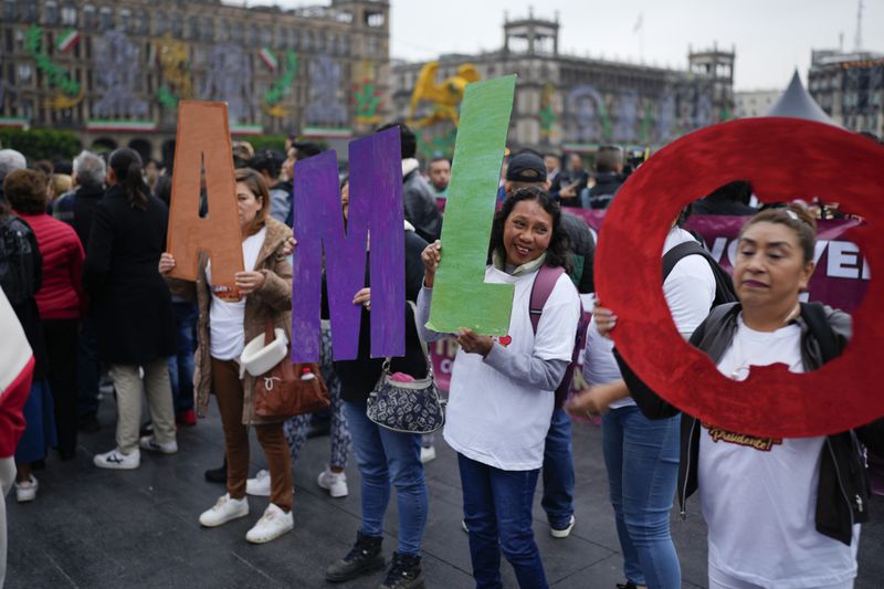 Supporters of Mexican President Andres Manuel Lopez Obrador hold up his initials outside the National Palace where he holds his last morning press conference, "La Mañanera," in Mexico City, Monday, Sept. 30, 2024. (AP Photo/Eduardo Verdugo)