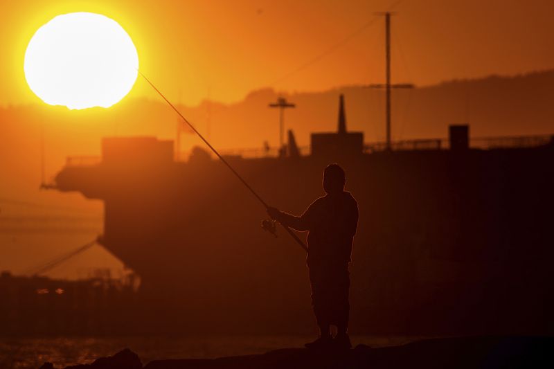 A man fishes off a jetty in Alameda, Calif., as the sun sets over the San Francisco Bay on Monday, July 1, 2024. An extended heatwave predicted to blanket Northern California has resulted in red flag fire warnings and the possibility of power shutoffs beginning Tuesday. (AP Photo/Noah Berger)