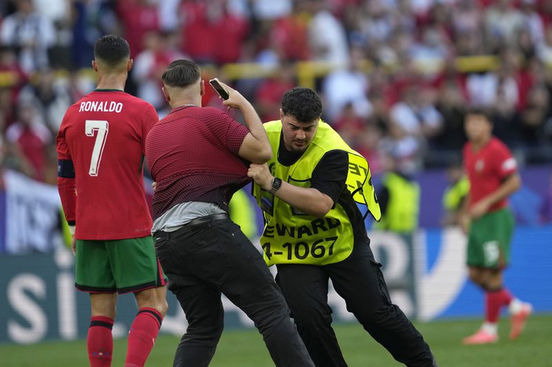 Steward catches a pitch invader that ran to Portugal's Cristiano Ronaldo during a Group F match between Turkey and Portugal at the Euro 2024 soccer tournament in Dortmund, Germany, Saturday, June 22, 2024. (AP Photo/Darko Vojinovic)